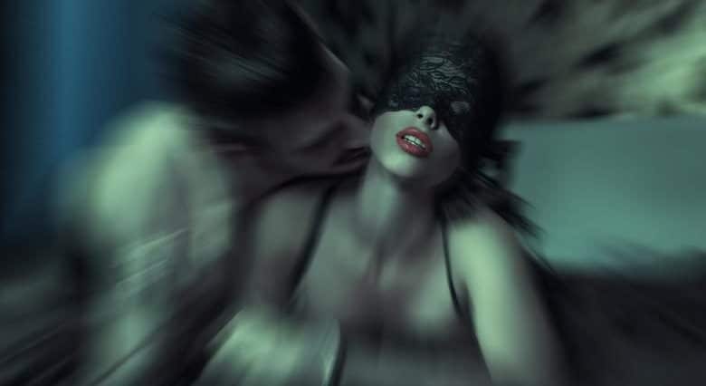 Artistic blurred photo of a blindfolded woman in lace lingerie with a partner leaning close to her neck