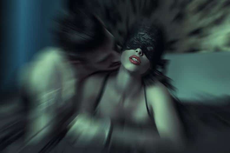 Artistic blurred photo of a blindfolded woman in lace lingerie with a partner leaning close to her neck