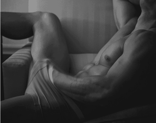 Black and white photo of a muscular man reclining with his hand inside his underwear