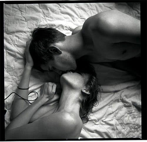 Black and white photo of a nude couple kissing on a bed