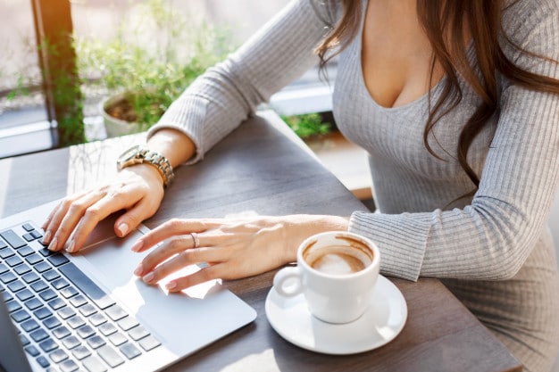 Woman in a grey top typing on a laptop at a cafe with a coffee