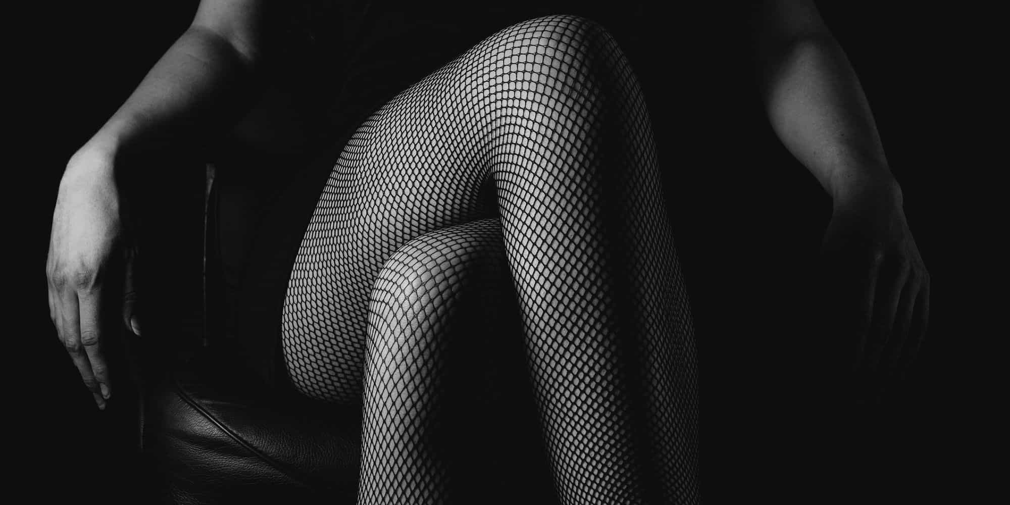 Black and white photo of a woman's crossed legs in fishnet stockings