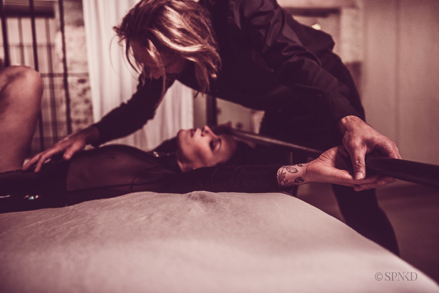 Dominant partner leaning over a restrained submissive in a dim BDSM scene