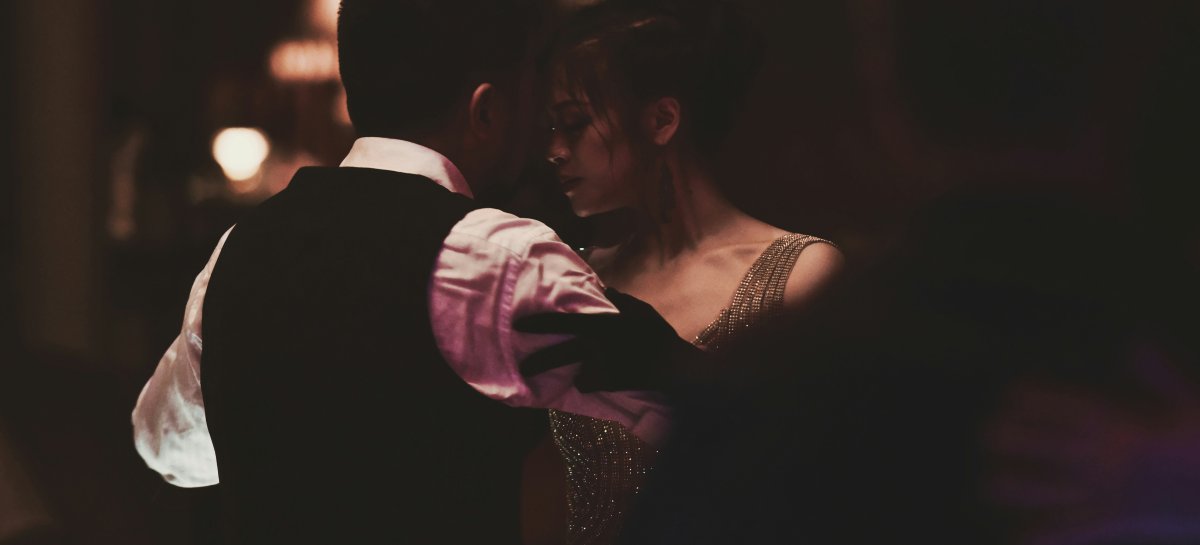 Couple dancing closely in dim, romantic light, woman in a sparkling gown