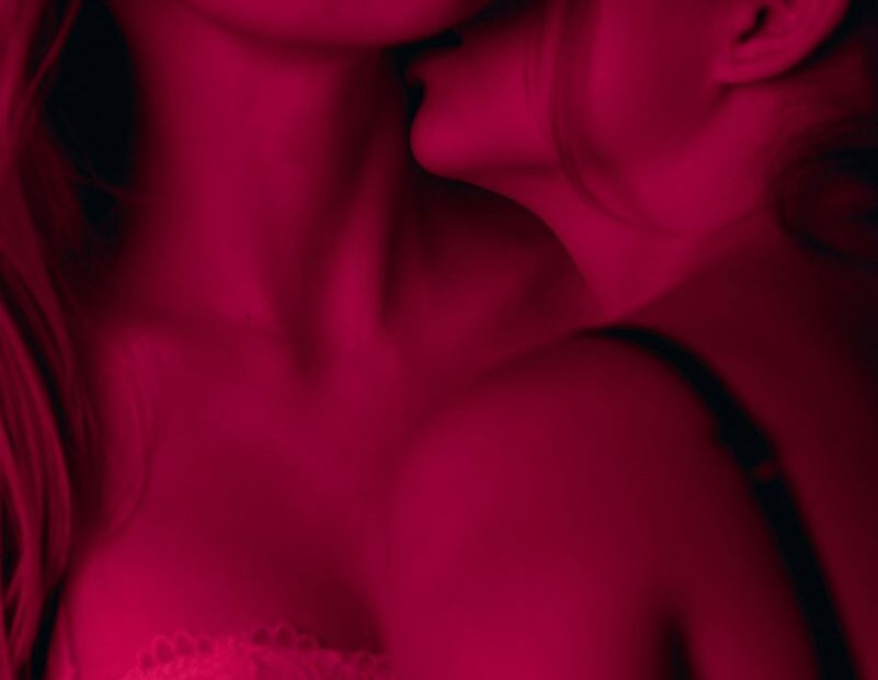Red-lit close-up of one partner kissing another's neck
