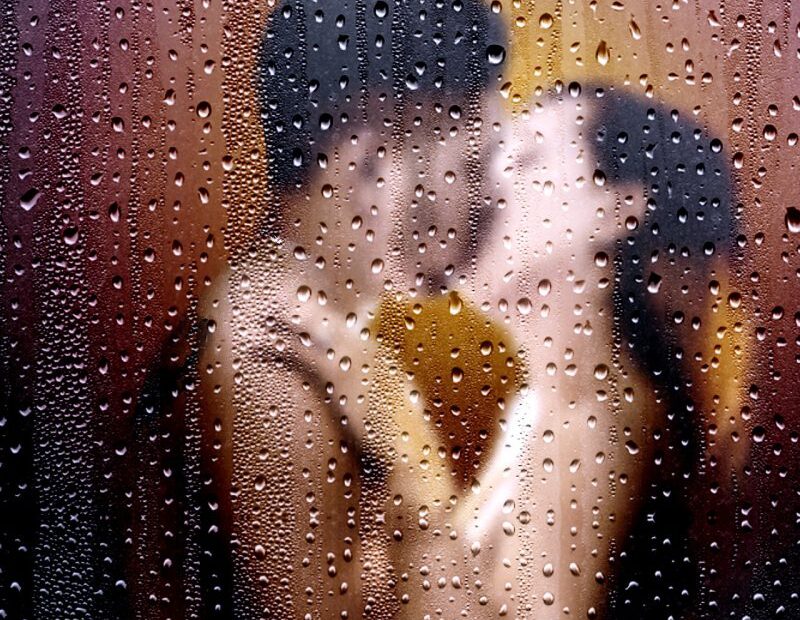 Couple embracing and kissing seen through a rain-covered glass window