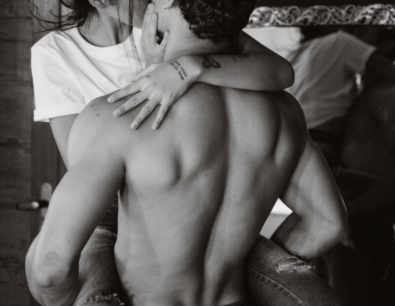 Black and white photo of a couple kissing, shirtless man lifting woman in jeans