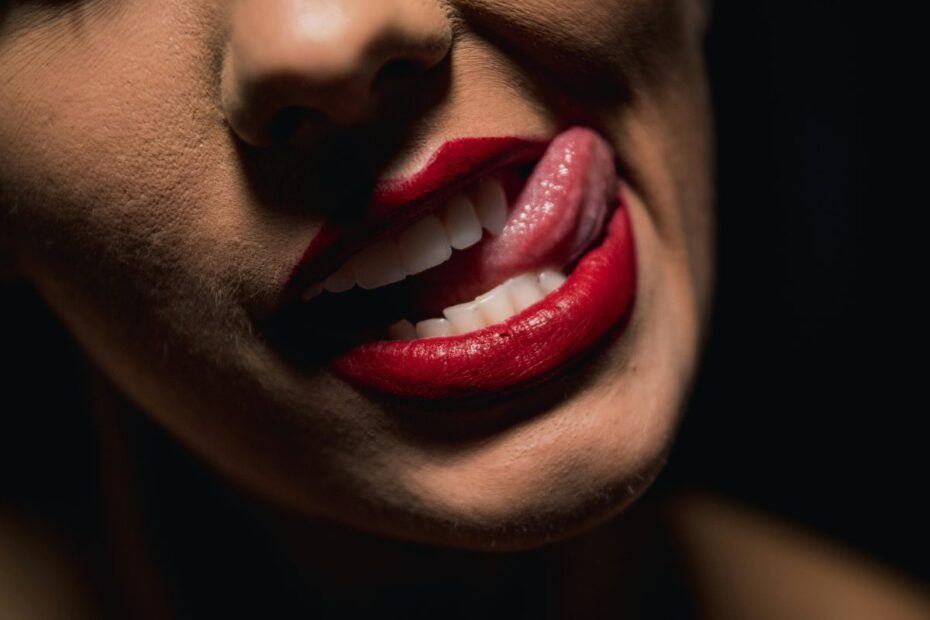 Close-up of a woman with red lipstick biting her lip and touching it with her tongue