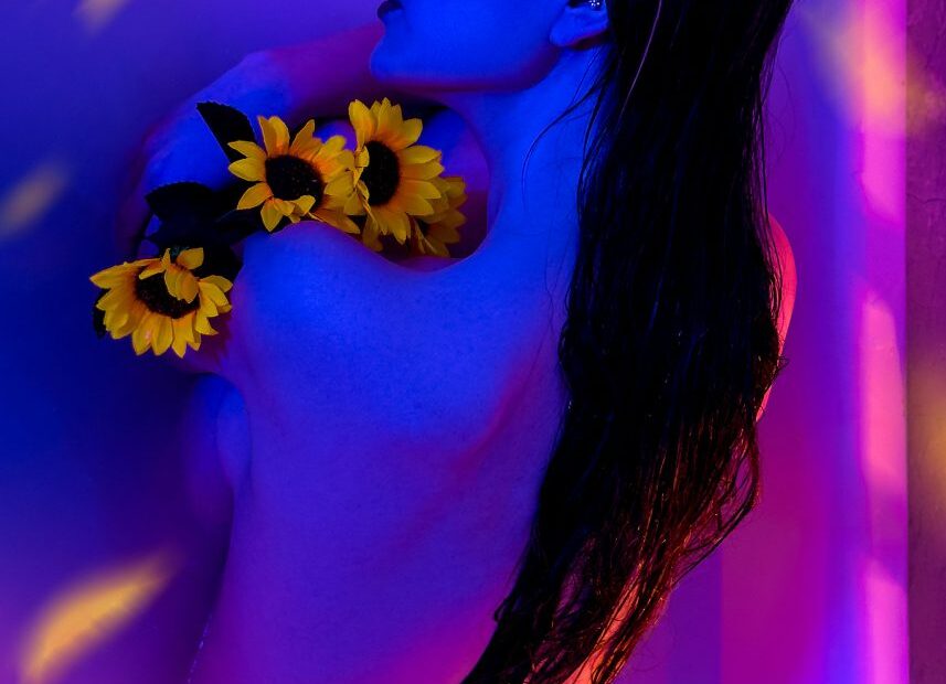 Nude woman seen from behind in blue and orange light, sunflowers over her shoulder