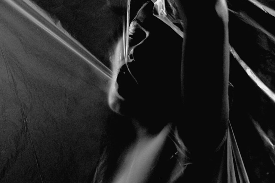 Black and white abstract photo of a woman's silhouette behind translucent plastic sheeting