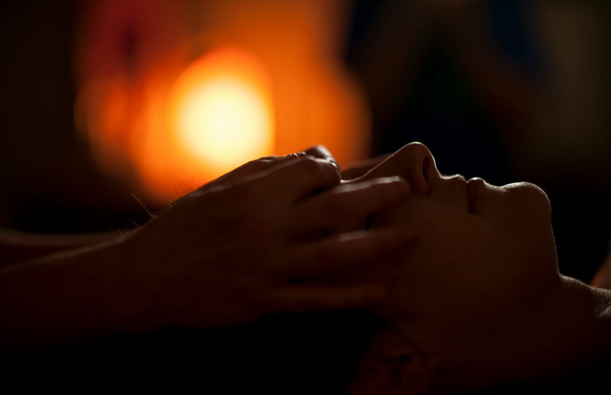 Hands giving a soothing face massage in warm candlelight