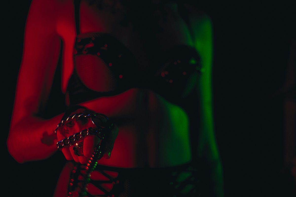 Woman in a studded bra holding a chain under red and green neon light