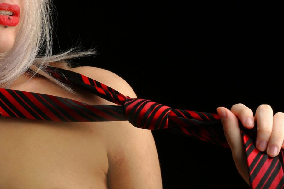 Woman with red lips pulling a red and black striped necktie across her bare chest
