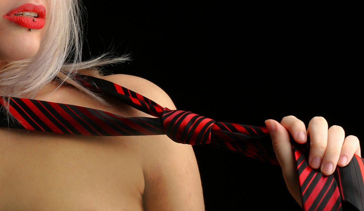 Woman with red lips pulling a red and black striped necktie across her bare chest