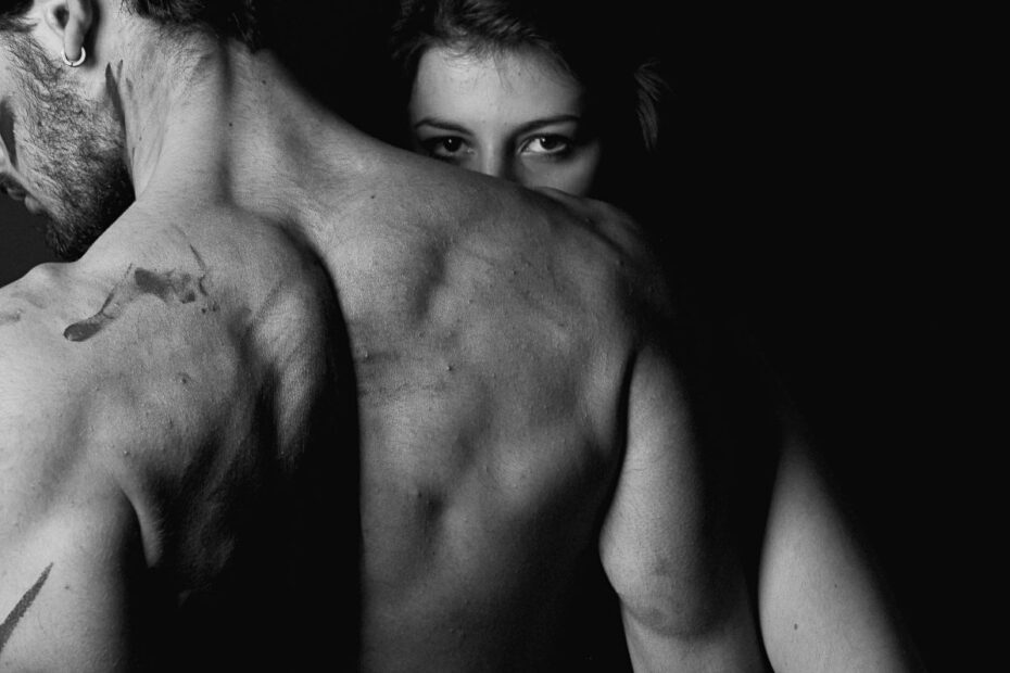 Black and white photo of a couple embracing, woman's eyes peering over a man's bare back