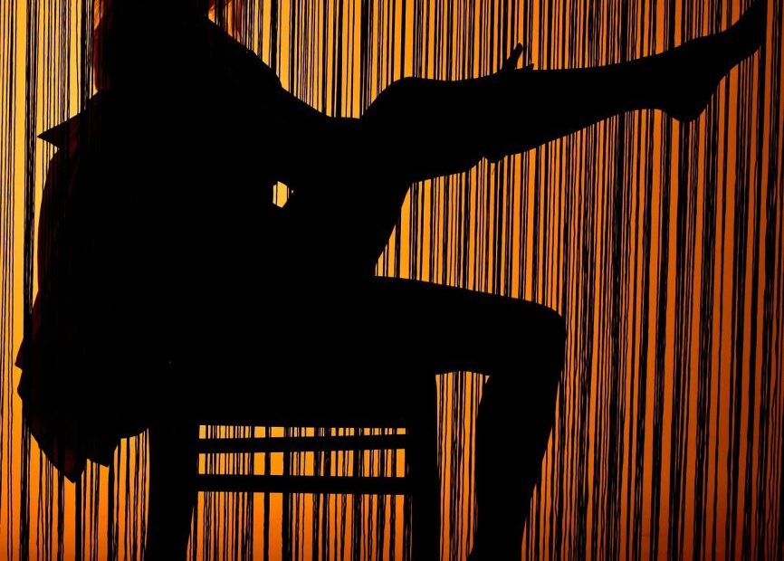 Silhouette of a woman seated and posing behind a backlit golden beaded curtain